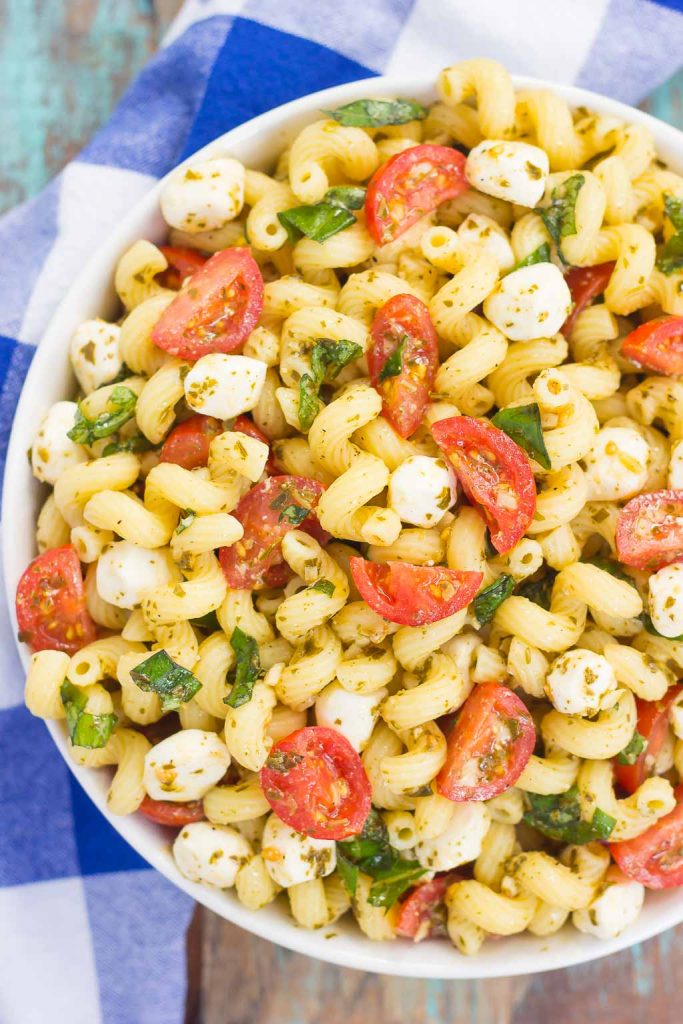 caprese pasta salad in white bowl on blue checked towel