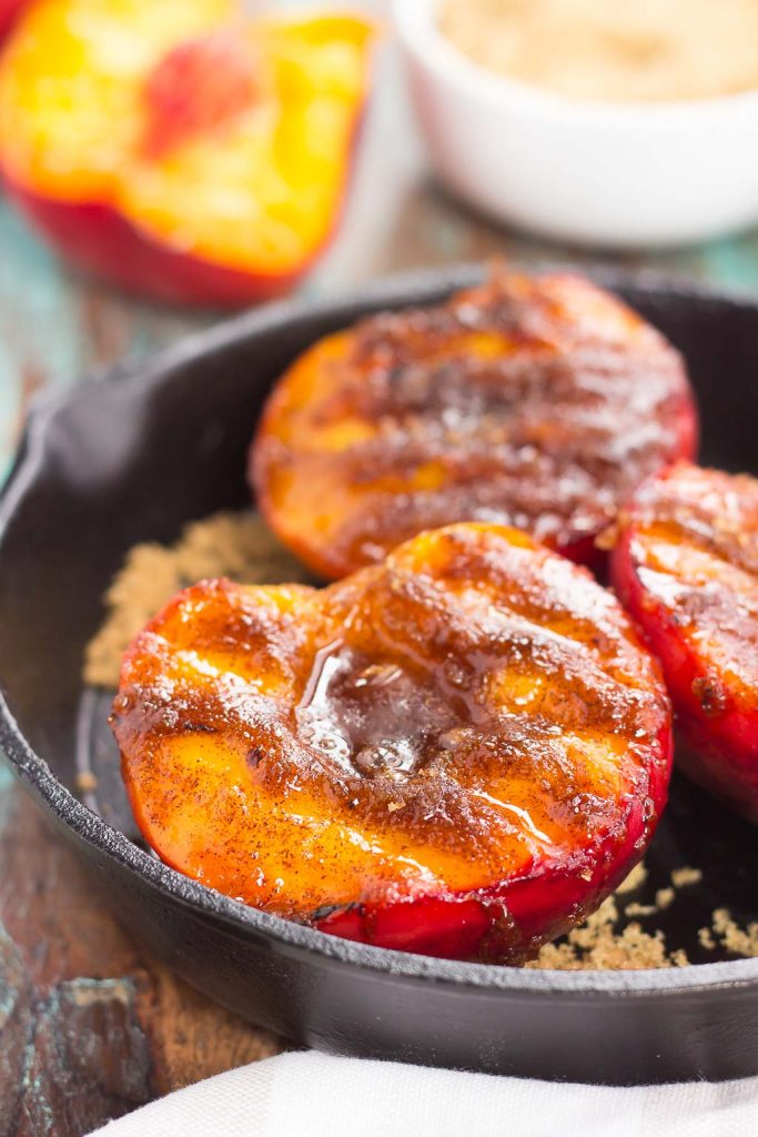 Three grilled peaches in a cast iron skillet.