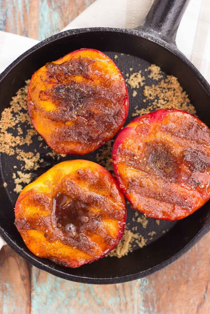 Overhead view of three caramelized peaches in a cast iron skillet. 