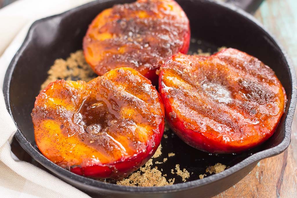 Three grilled peaches in a cast iron skillet. 