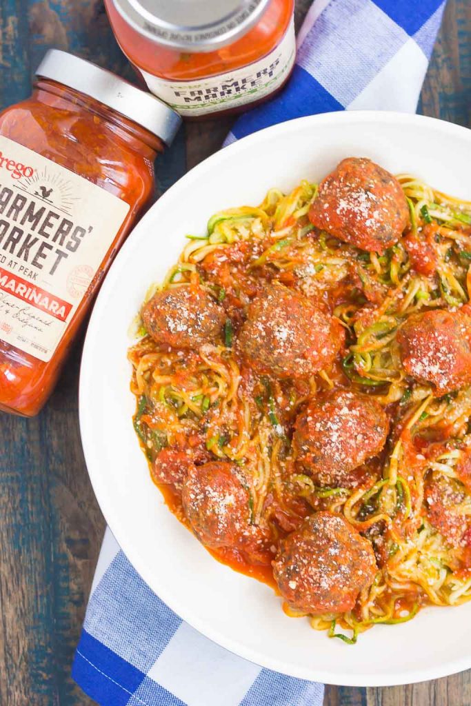 Overhead view of a skillet of zoodles and meatballs next to two jars of pasta sauce. 