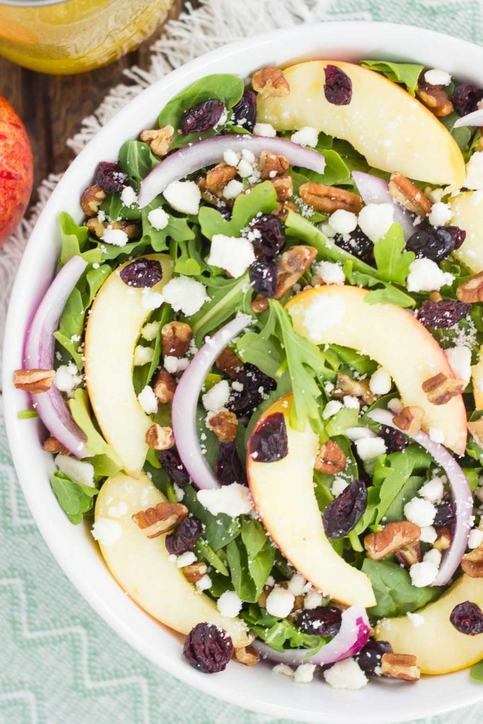 overhead view of an apple pecan salad with cranberries in a large white bowl 