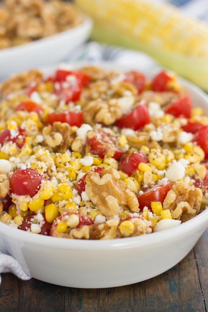 sweet corn salad with walnuts and tomatoes in a white serving platter. 