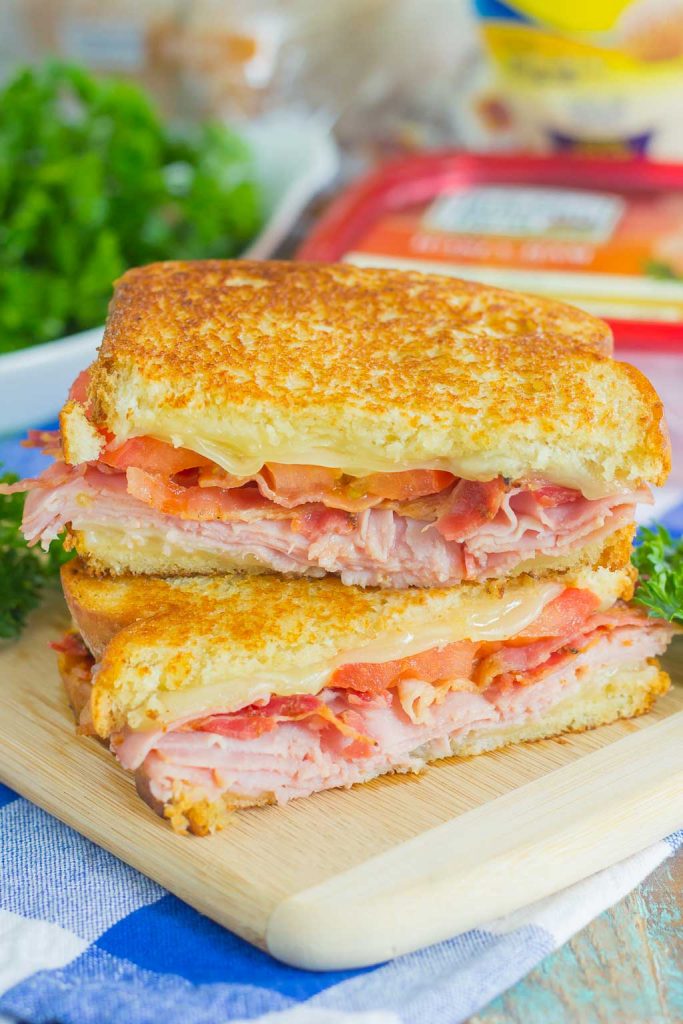 a grilled ham and cheese sandwich sliced in half and stacked on a cutting board