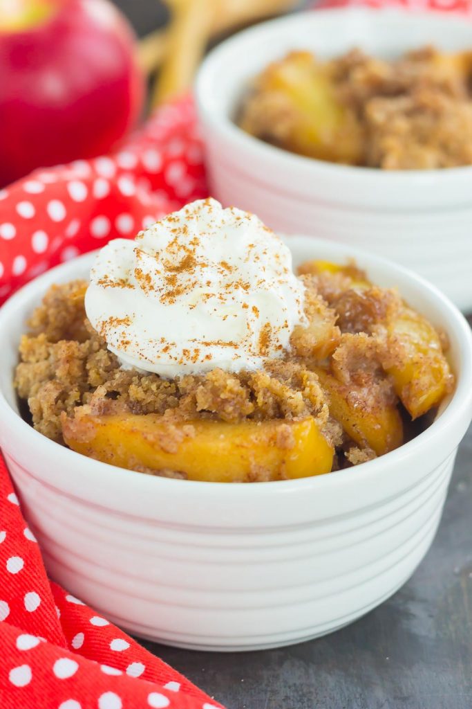 serving of apple cobbler dump cake in a white bowl. whipped cream has been piped on top. 