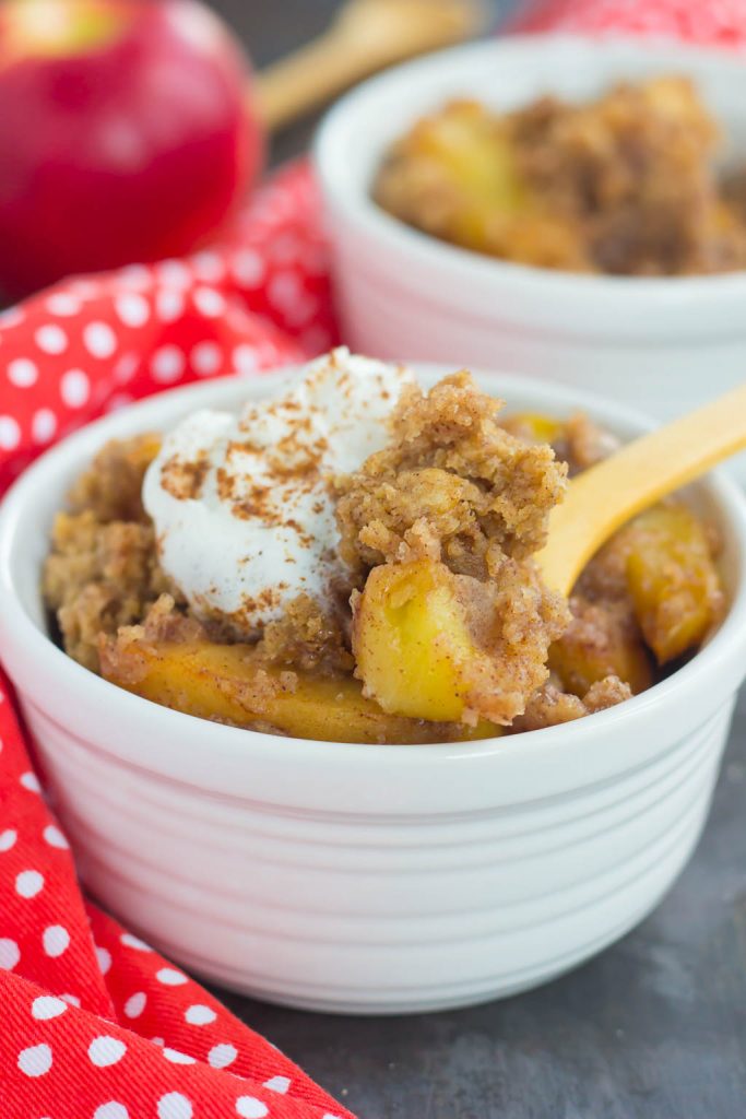 slow cooker apple cobbler dump cake in a white bowl with whipped cream and a wood spoon. 