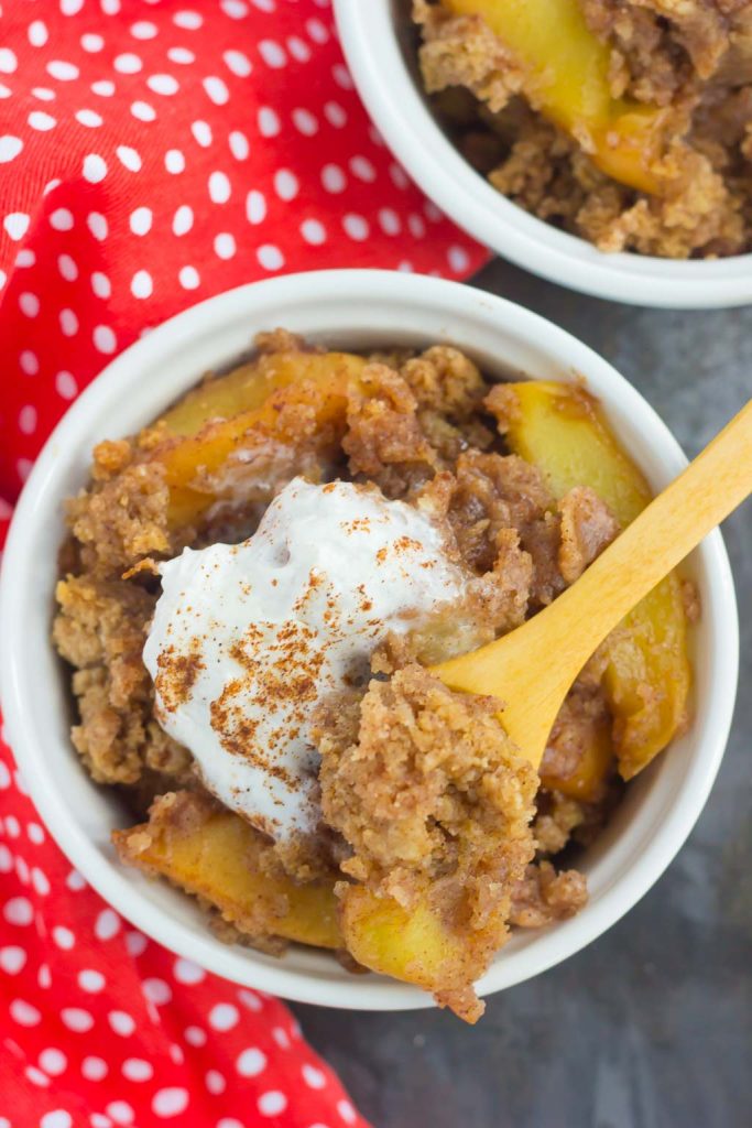 overhead view of crockpot apple dump cake garnished with whipped cream in a white bowl. A wood spoon rests on top. 