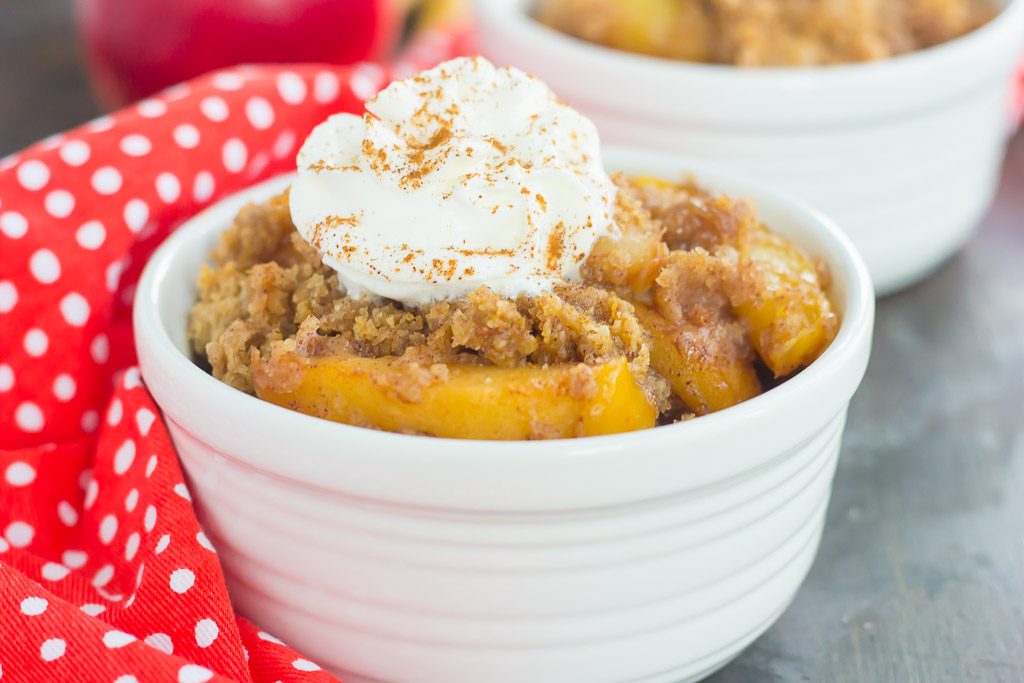 close up of serving of crockpot dump cake garnished with whipped cream in a white bowl. 