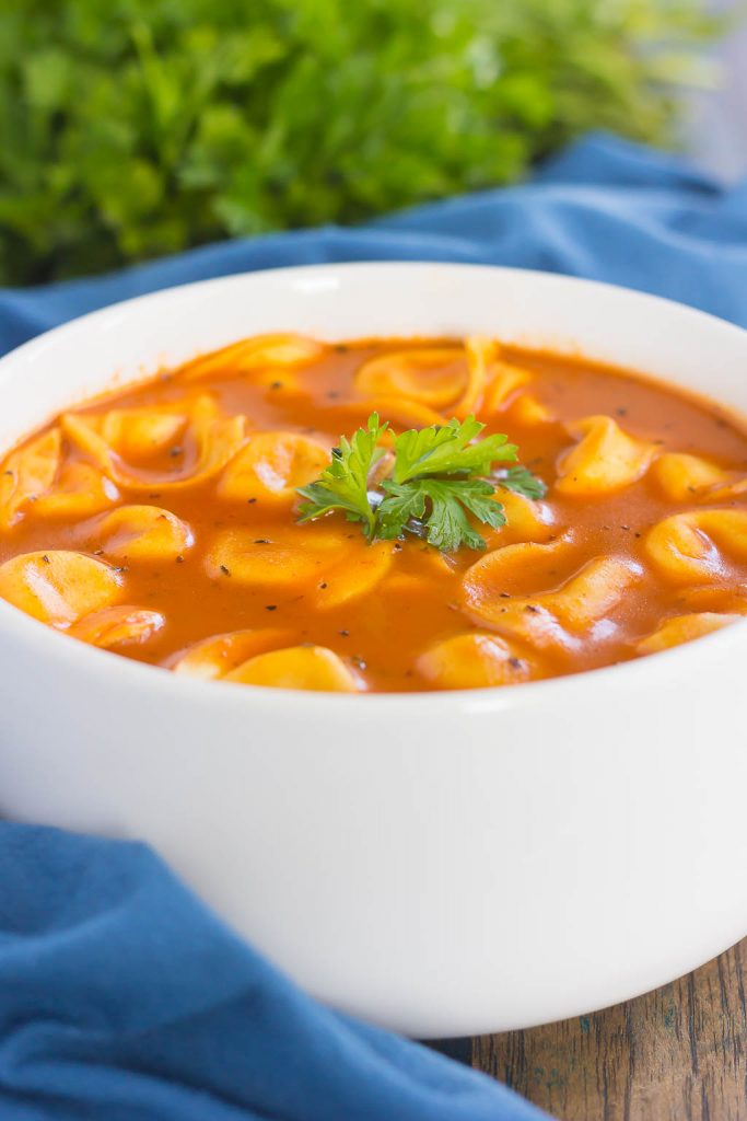 bowl of creamy tomato tortellini soup. a blue towel and fresh parsley rests in the background