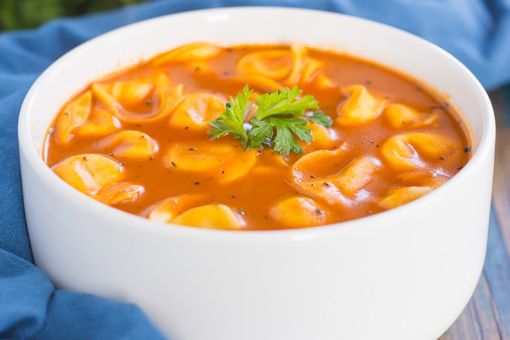 bowl of tomato basil tortellini soup next to a blue towel 