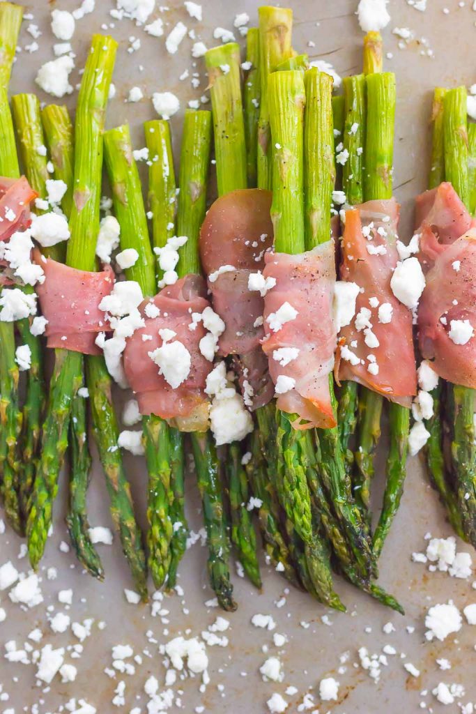 overhead view of prosciutto wrapped asparagus sprinkled with feta on a baking sheet