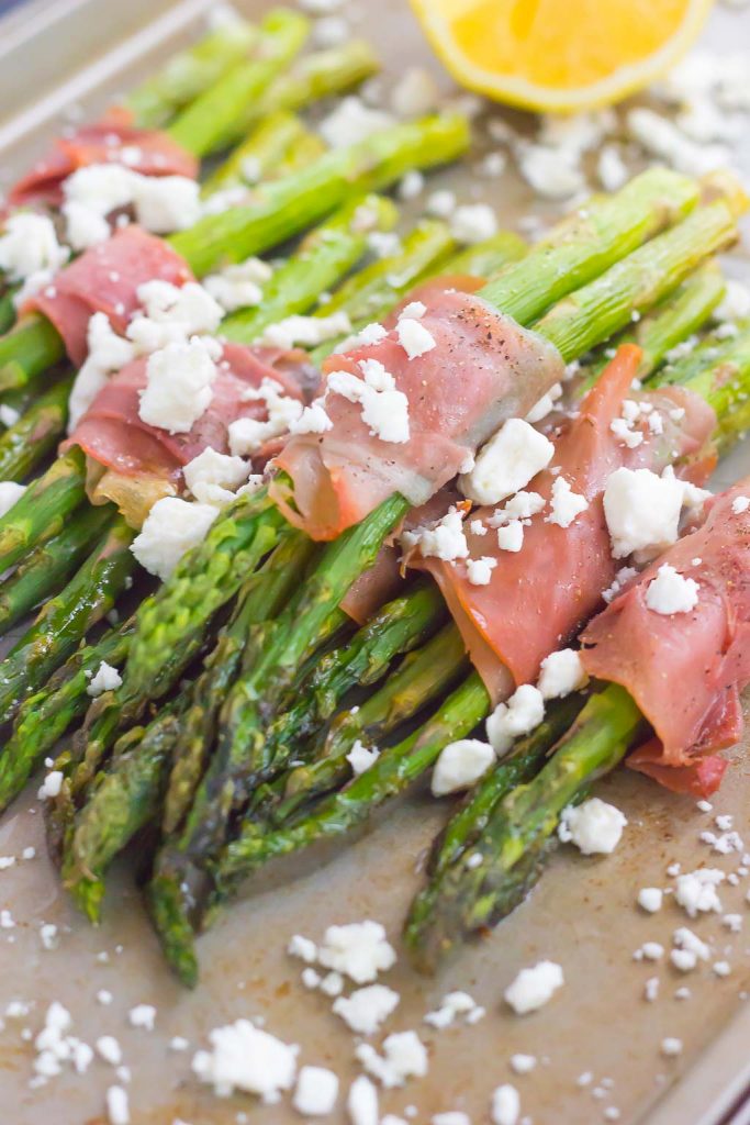 prosciutto wrapped asparagus sprinkled with feta on a baking sheet