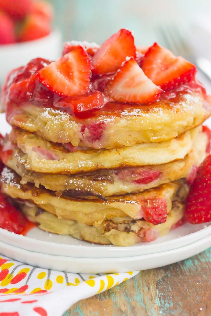 A stack of fluffy strawberry pancakes topped with strawberry sauce. 