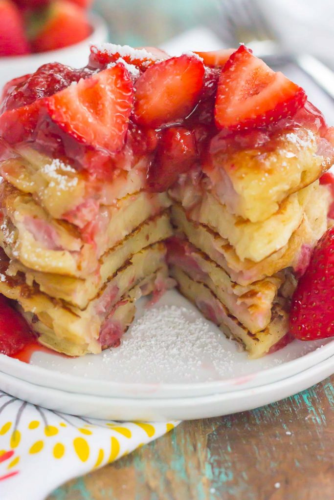 A stack of fluffy strawberry pancakes topped with strawberry sauce. A portion has been cut from the stack. 