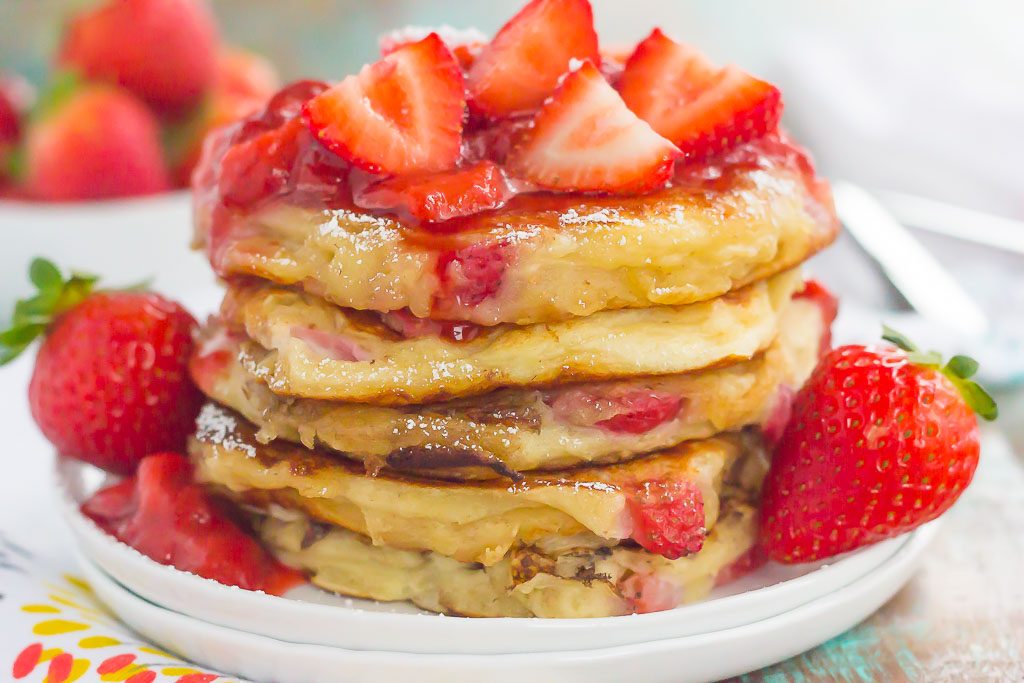 A stack of fluffy strawberry pancakes topped with strawberry sauce. 