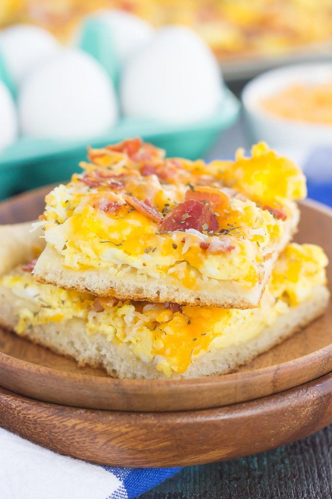 Two slices of a bacon and eggs breakfast pizza on a stack of wooden plates. 