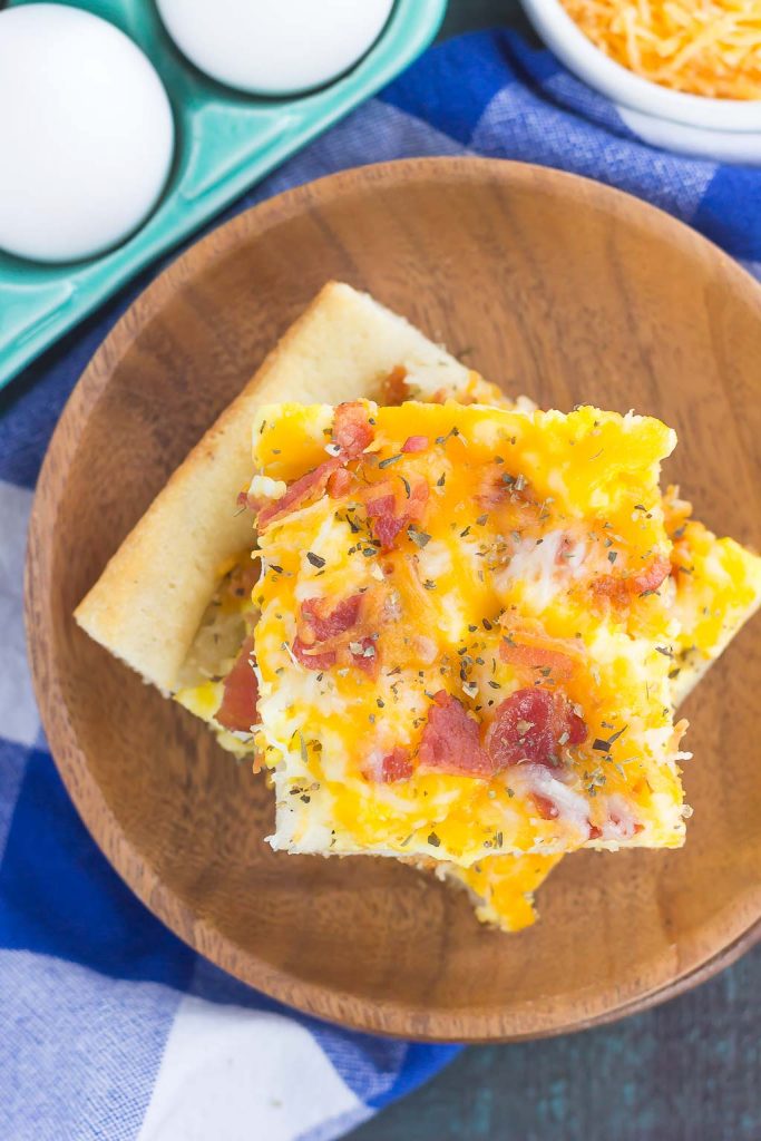 Two slices of a bacon and eggs breakfast pizza on a stack of wooden plates. 