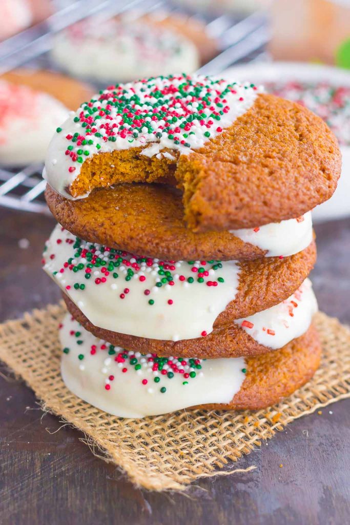 A stack of four soft gingersnap cookies dipped in white chocolate. The top cookie is missing a bite. 