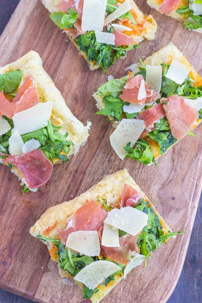 This Arugula and Prosciutto Puff Pastry Pizza is easy to make and ready in about 20 minutes. Puff pastry dough is drizzled with olive oil, and then topped with mozzarella cheese, fresh arugula, salty prosciutto and some shaved Parmesan cheese. Simple, fresh, and bursting with flavor, this lighter pizza is perfect for busy weeknights and is sure to be a mealtime winner