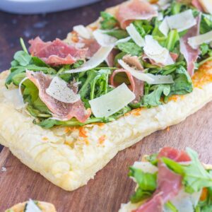 This Arugula and Prosciutto Puff Pastry Pizza is easy to make and ready in about 20 minutes. Puff pastry dough is drizzled with olive oil, and then topped with mozzarella cheese, fresh arugula, salty prosciutto and some shaved Parmesan cheese. Simple, fresh, and bursting with flavor, this lighter pizza is perfect for busy weeknights and is sure to be a mealtime winner