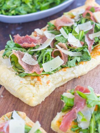 This Arugula and Prosciutto Puff Pastry Pizza is easy to make and ready in about 20 minutes. Puff pastry dough is drizzled with olive oil, and then topped with mozzarella cheese, fresh arugula, salty prosciutto and some shaved Parmesan cheese. Simple, fresh, and bursting with flavor, this lighter pizza is perfect for busy weeknights and is sure to be a mealtime winner