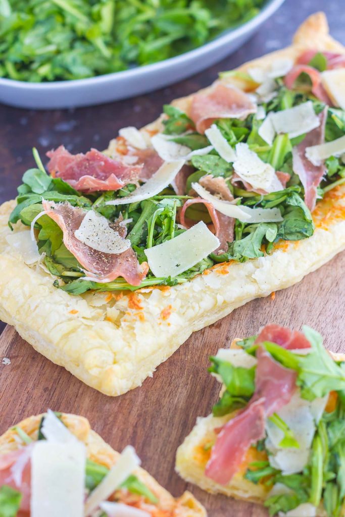 This Arugula and Prosciutto Puff Pastry Pizza is easy to make and ready in about 20 minutes. Simple, fresh, and bursting with flavor, this lighter pizza is perfect for busy weeknights and is sure to be a mealtime winner! #pizza #puffpastry #puffpastrypizza #arugula #arugulapizza #prosciutto #prosciuttopizza #pizzarecipe #dinner #easydinner