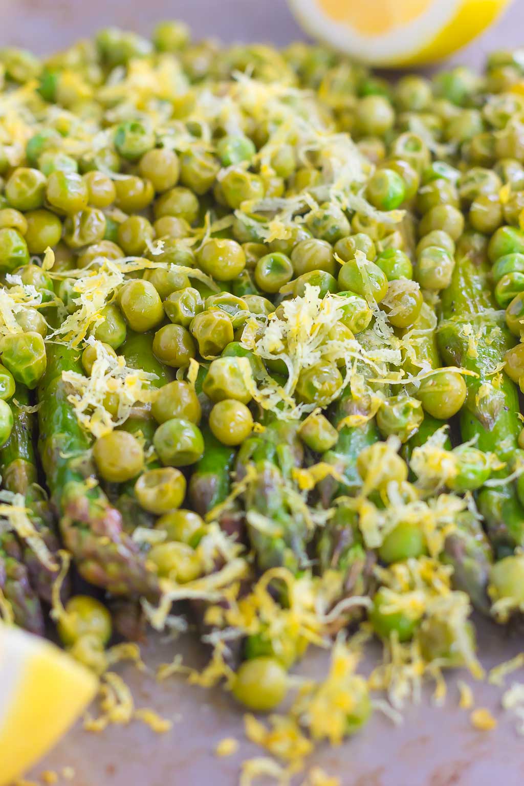 roasted asparagus with lemon and peas on a baking sheet. Lemon wedges rest in the background.