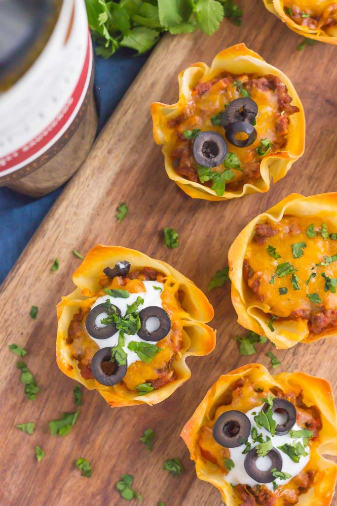 Overhead view of baked wonton taco cups on a wooden serving board. 