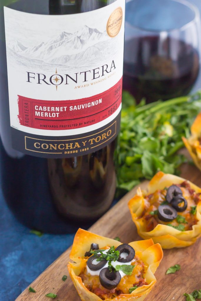 Mini taco bites on a wood board next to a bottle of Frontera wine. 