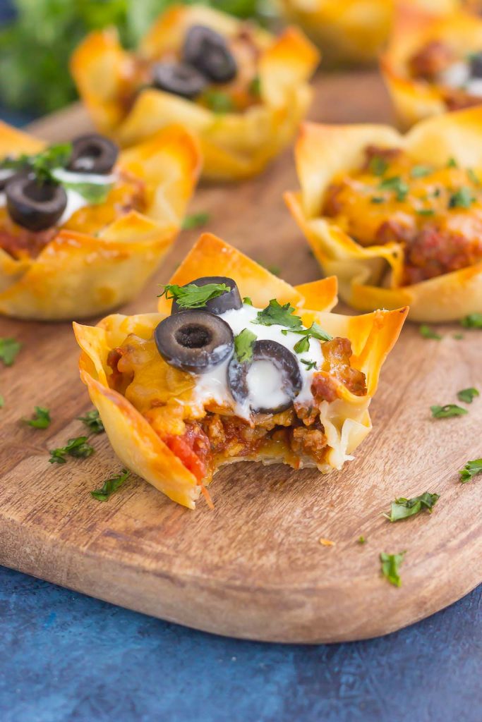 mini taco cups on a wood serving board. The front taco cup has a bite missing. 