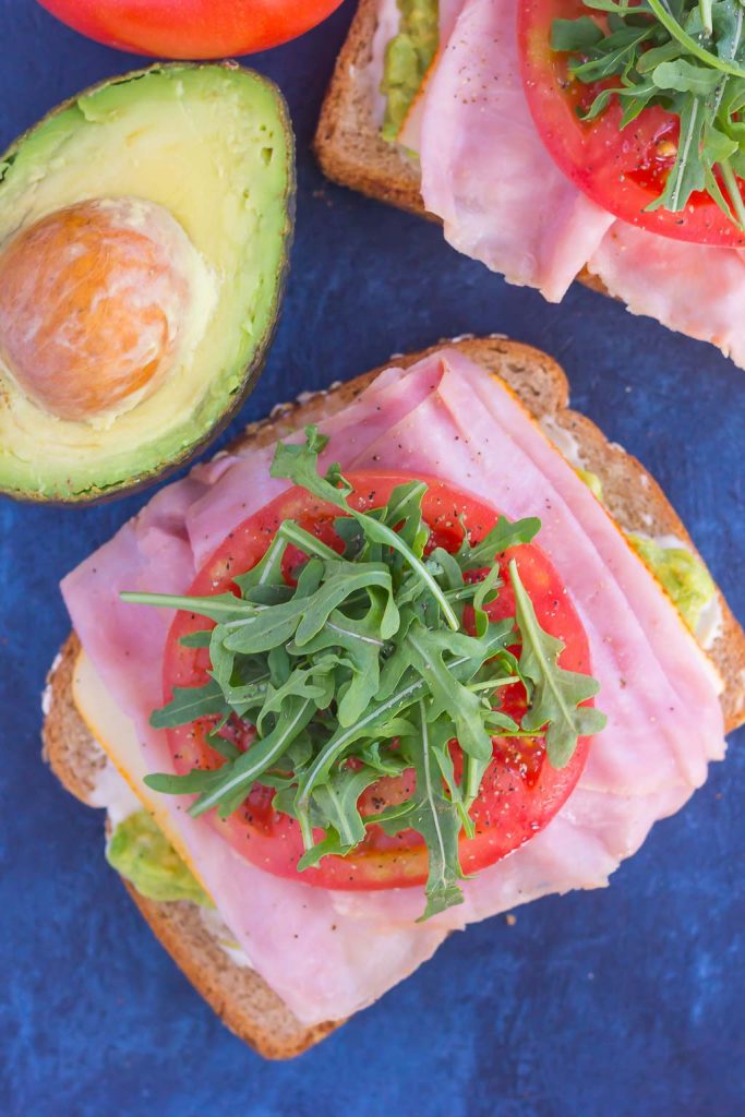 overhead view of a honey baked ham open faced sandwich next to an avocado half 