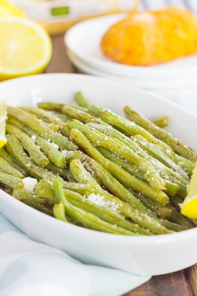 A white serving dish of lemon garlic green beans. Lemon halves rest in the background. 