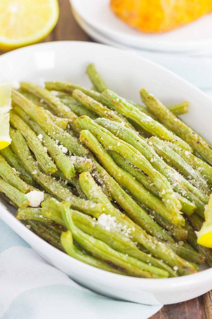 A white serving dish of lemon garlic green beans. Lemon halves rest in the background. 