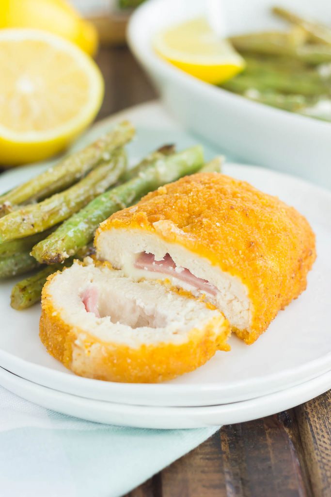 A serving of chicken cordon bleu on a white plate alongside roasted fresh green beans. 