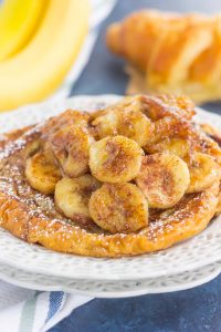 serving of croissant french toast topped with caramelized bananas on a white plate 