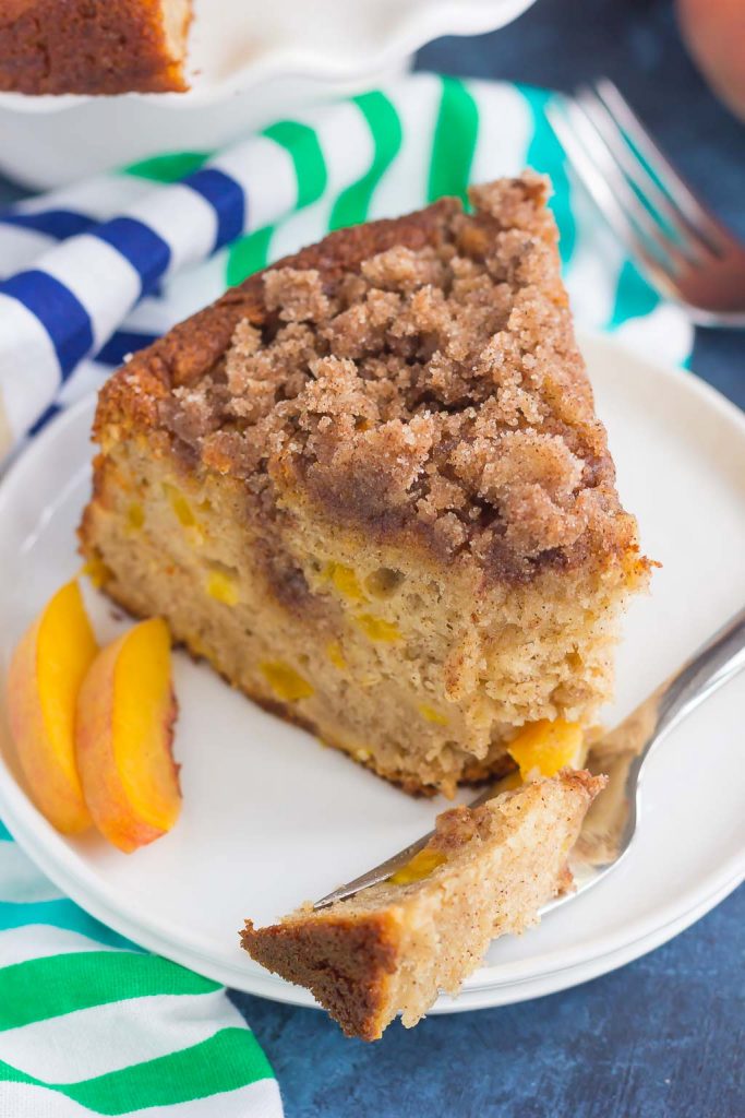 A slice of fresh peach cake on a white plate, with a piece on a fork. 