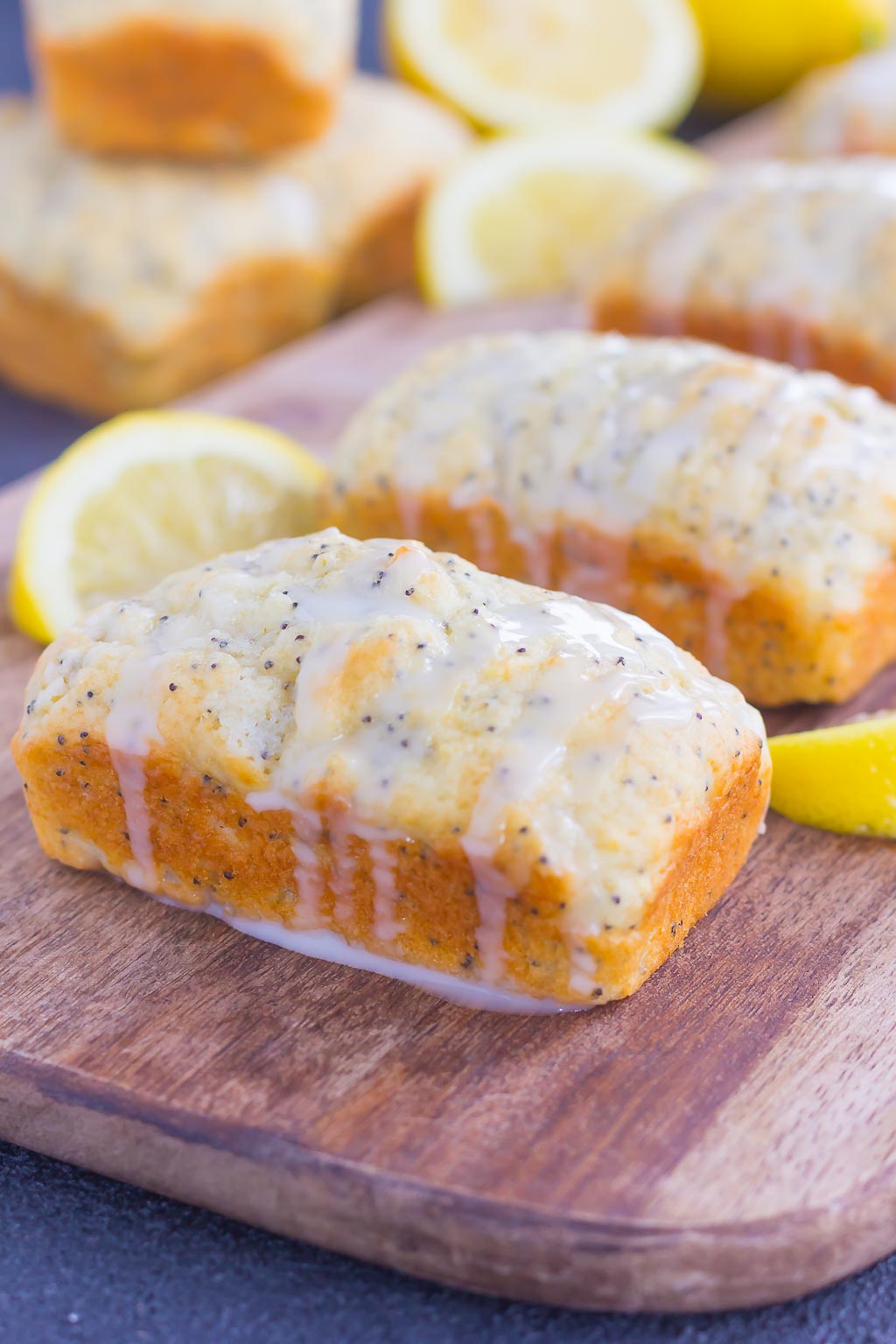 mini loaves of lemon poppy seed bread with glaze on a wood board with lemon wedges 