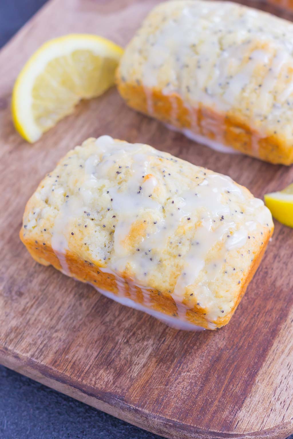 two mini loaves of lemon poppy seed bread with glaze on a wood board 