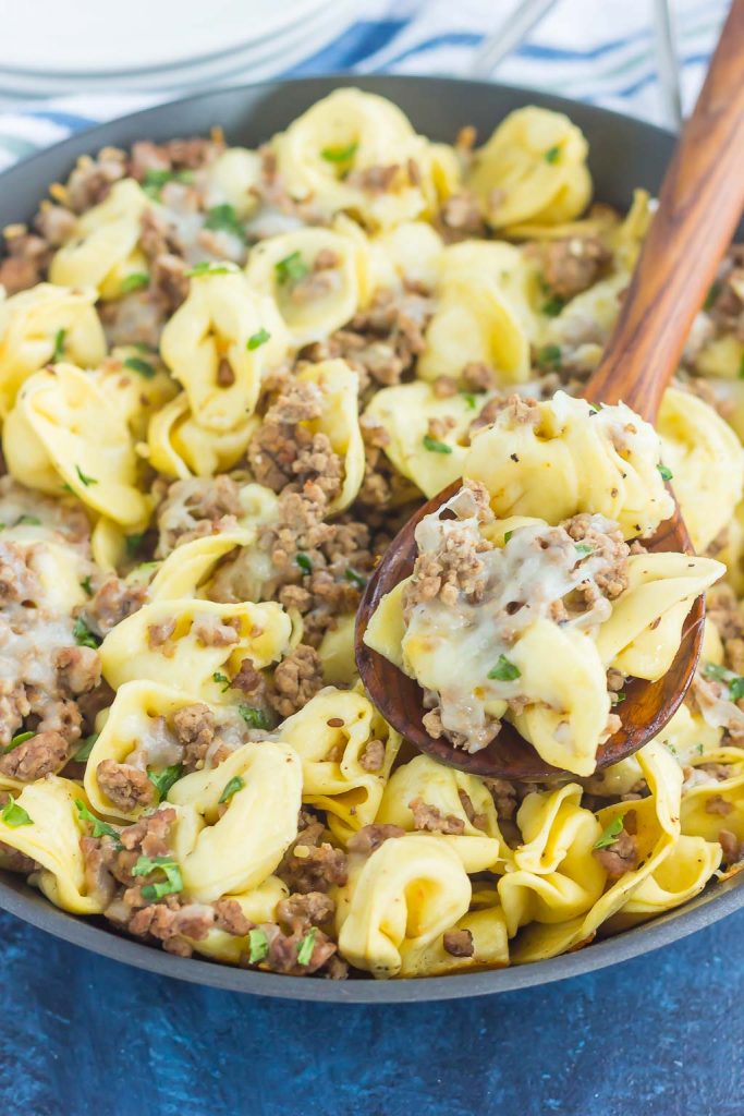 a skillet of ground beef tortellini. a wooden spoon is holding up a serving. 