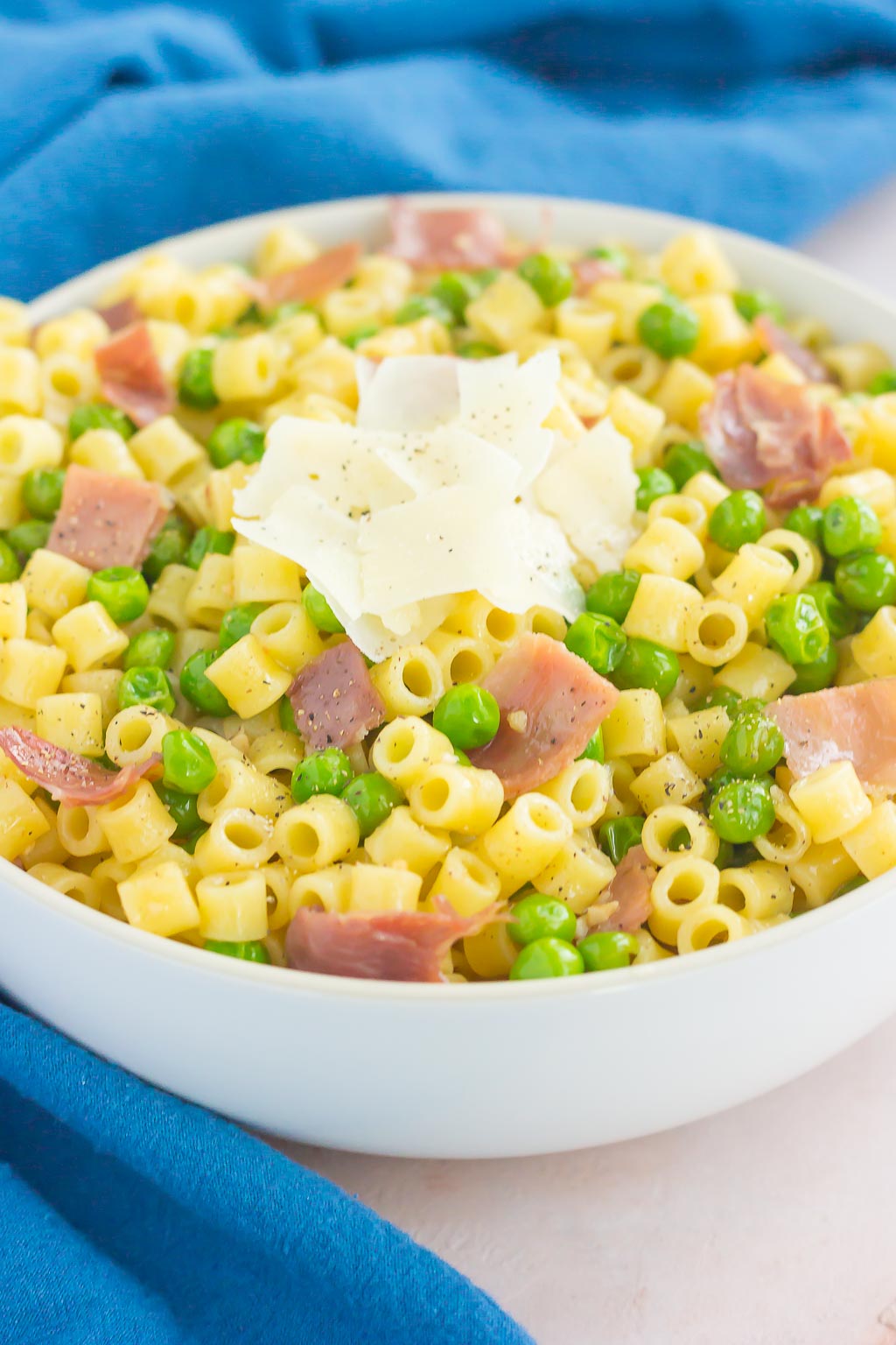 A large white bowl of pasta with peas and prosciutto. 