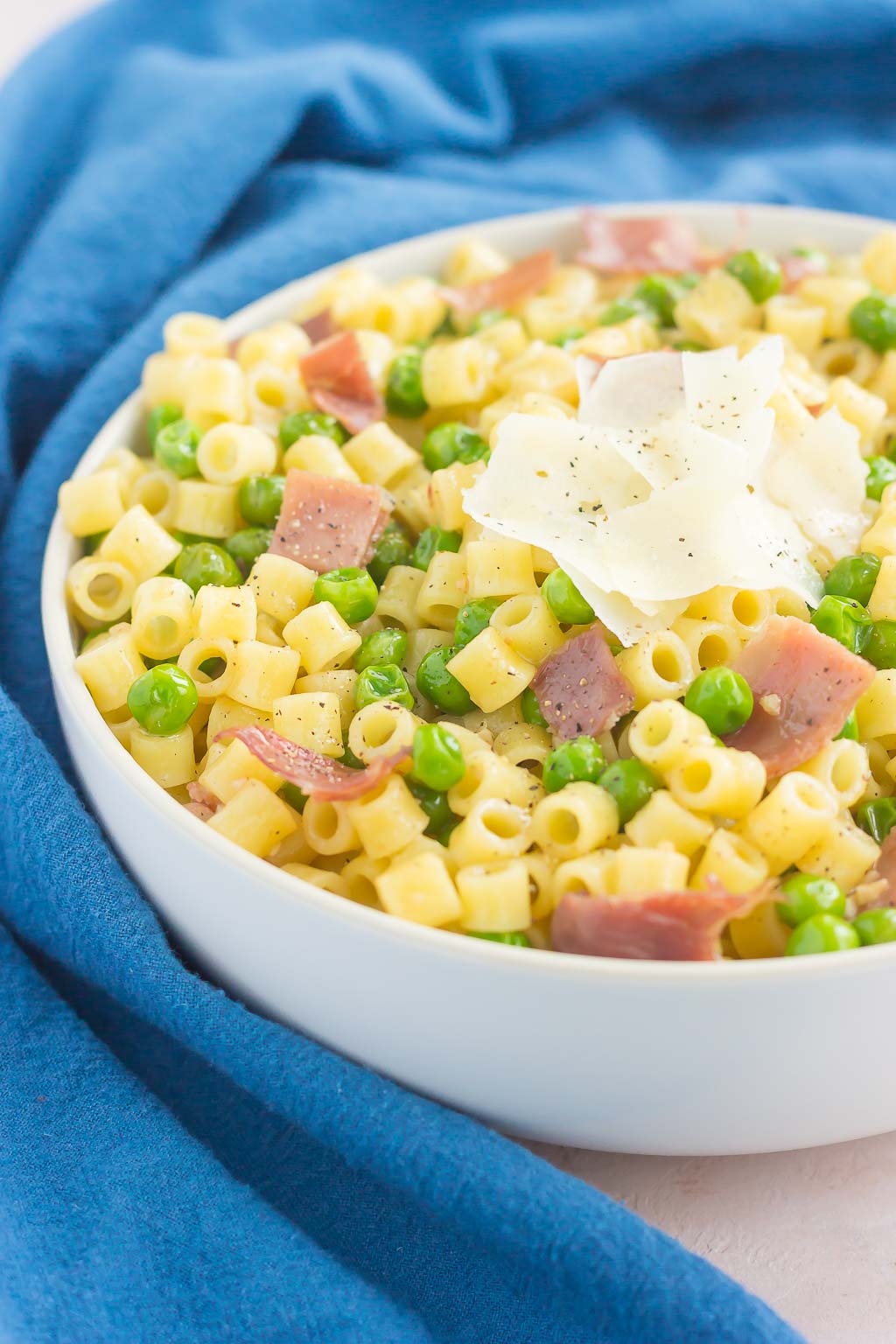 A large white bowl of pasta with peas and prosciutto. 