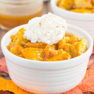 pumpkin bread pudding in a white bowl with a dollop of whipped cream