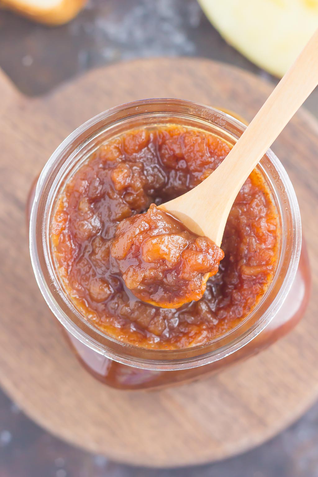 overhead view of homemade apple butter in a glass jar with a wooden spoon resting on top