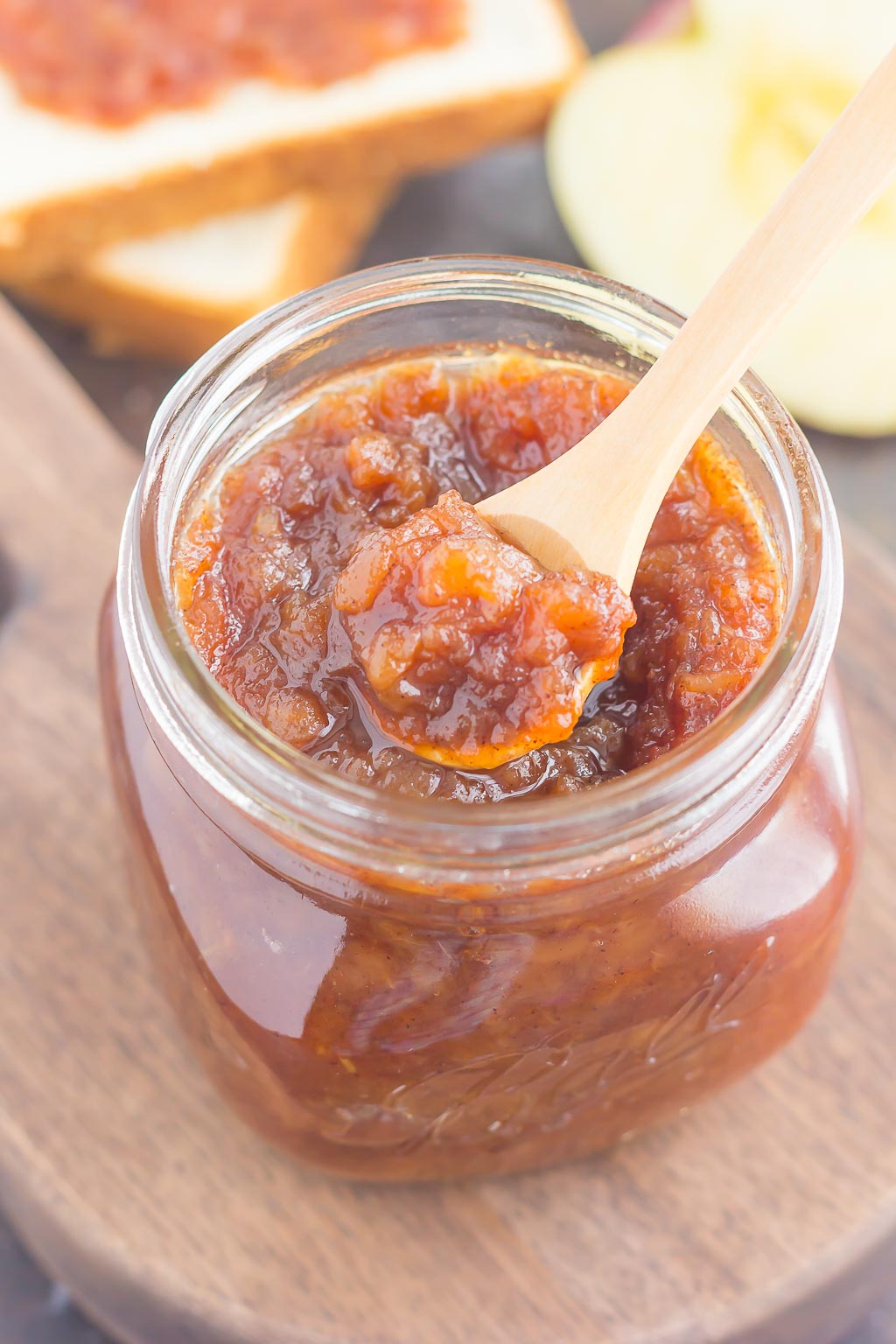 glass jar of slow cooker apple butter with a wooden spoon resting on top 