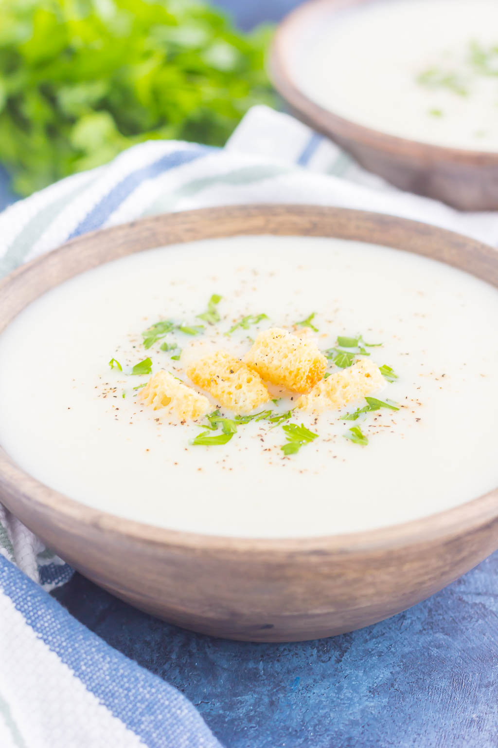 Two bowls of cauliflower parmesan soup, garnished with parsley and croutons. 