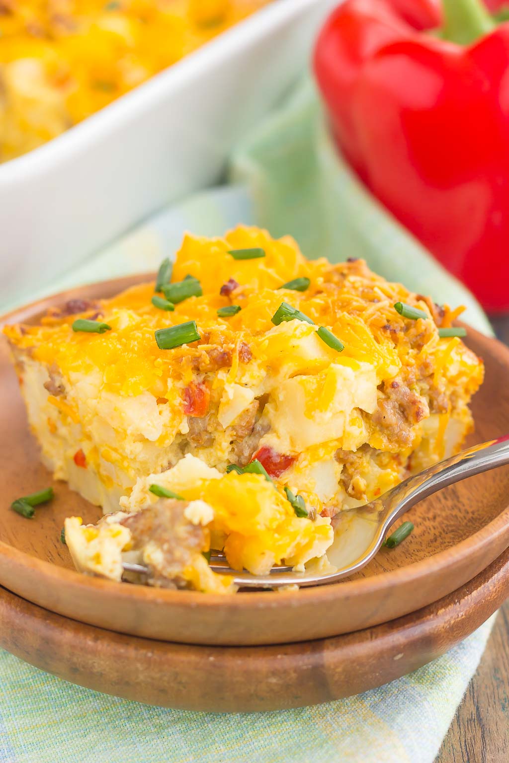 a slice of sausage hashbrown breakfast casserole on a wooden plate with a fork. 