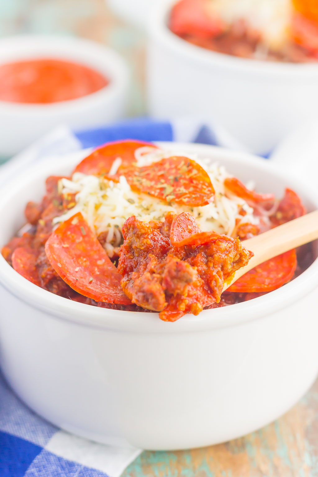 Side view of a white ramekin filled with slow cooker no bean chili, topped with cheese and pepperoni slices. 