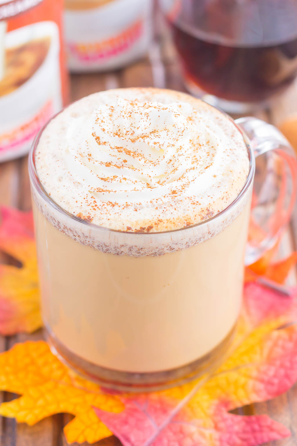 A maple latte garnished with whipped cream in a glass mug. 