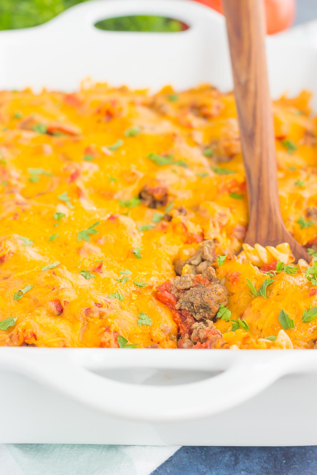 cheesy ground beef pasta casserole in white casserole dish with serving spoon