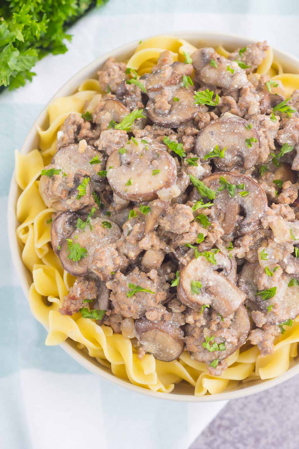 Top view of a A bowl of ground beef stroganoff atop a bed of buttered egg noodles. 